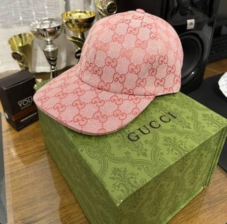 Ροζ καπέλο Gucci πάνω σε πράσινο κουτί Gucci, με κύπελλα στο βάθος