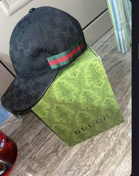Μαύρο καπέλο Gucci ακουμπισμένο σε πράσινο κουτί Gucci