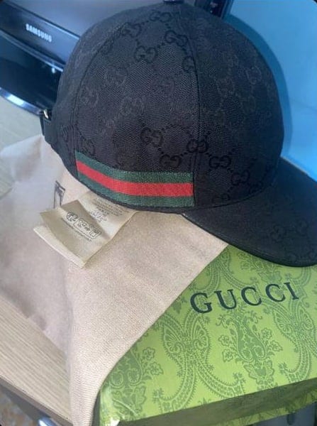 Μαύρο καπέλο Gucci πάνω σε υφασμάτινη θήκη και πράσινο κουτί Gucci