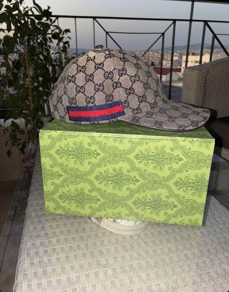 Καπέλο Gucci πάνω σε πράσινο κουτί Gucci, σε ταράτσα με θέα την πόλη