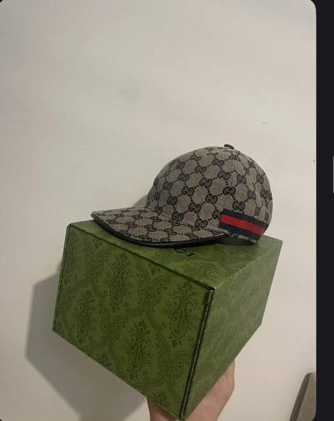 Καπέλο Gucci με μονόγραμμα ακουμπισμένο σε πράσινο κουτί Gucci
